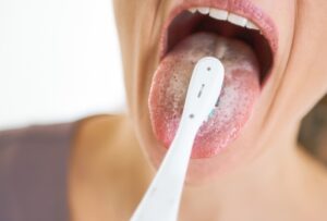 Closeup On Young Woman Cleaning Tongue Using Toothbrush